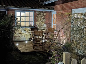 A patio with a table and chairs, a stone wall, and a window with blinds. - Gables Cottage, Market Rasen (Market Rasen)