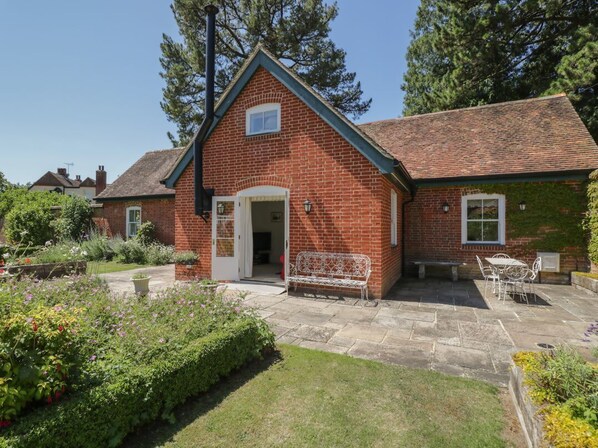 A brick house with a front door, a small porch, and a garden with flowers and shrubs.