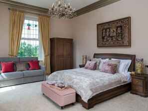 A bedroom with a large bed, a sofa, a wooden cabinet, a chandelier, and a large framed picture on the wall. - Moorlands Manor, in Foulridge. (Colne)