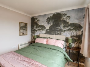 A bedroom with a bed, a nightstand, a lamp, a painting, and a window with curtains.
