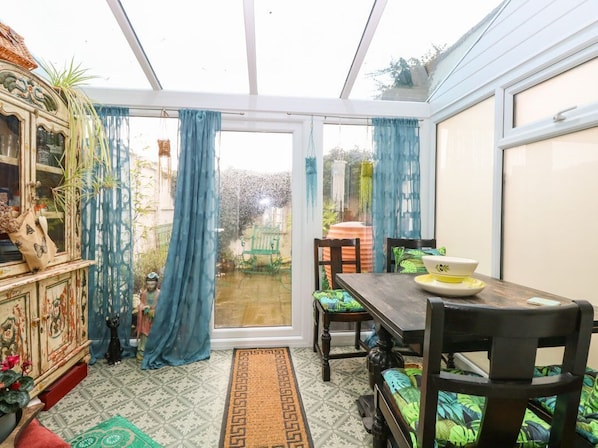 A conservatory with a dining table, chairs, and a view of the garden.