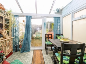 A conservatory with a dining table, chairs, and a view of the garden.