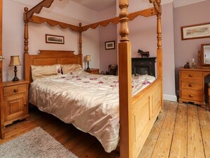 A four-poster bed with a wooden frame, a bedside table with a lamp, a dresser, and a fireplace.