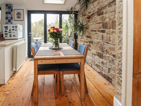 A dining area with a wooden table, chairs, a vase with flowers, and a stone wall.