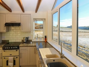 Una cocina con estufa, horno y ventanas amplias que dan a un paisaje rural.