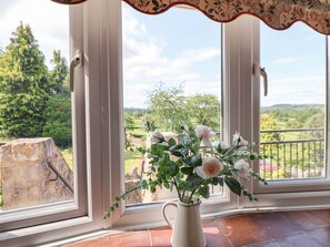 A white vase with flowers on a windowsill, a view of greenery and a stone structure outside. - The Old Barn, Pentre Celyn (Ruthin)