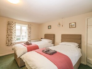 A hotel room with two beds, a window with curtains, a light fixture, and a door.