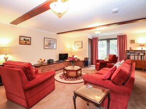 A living room with red sofas, a fireplace, a television, and a bookshelf. - Walnut Tree Cottage, Catfield (Great Yarmouth)