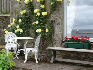 A stone wall with yellow flowers, a white metal bench, and a table with chairs. - The Lookout, Berwick-Upon-Tweed (Berwick-upon-Tweed)