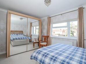 Un dormitorio con cama, una silla, un armario con espejo y una ventana con cortinas.