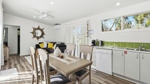 A modern kitchen with white cabinets, a dining table with chairs, a ceiling fan, and a large mirror on the wall. - Seabush Retreat - Phillip Island - Resort Facilities (Cowes)