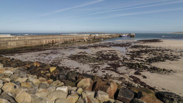 A coastal view with a rocky shoreline, a concrete breakwater, and a boat docked at the pier. - Cabin 2 Min Larach (Gortahork)