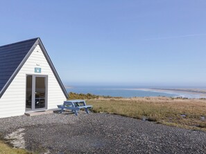 A small white building with a door and a window, a picnic table, and a view of the ocean. - Cabin 2 Min Larach (Gortahork)