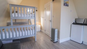 A room with a bunk bed, a white radiator, a small kitchenette, and a door leading to another room. - Cabin 2 Min Larach (Gortahork)
