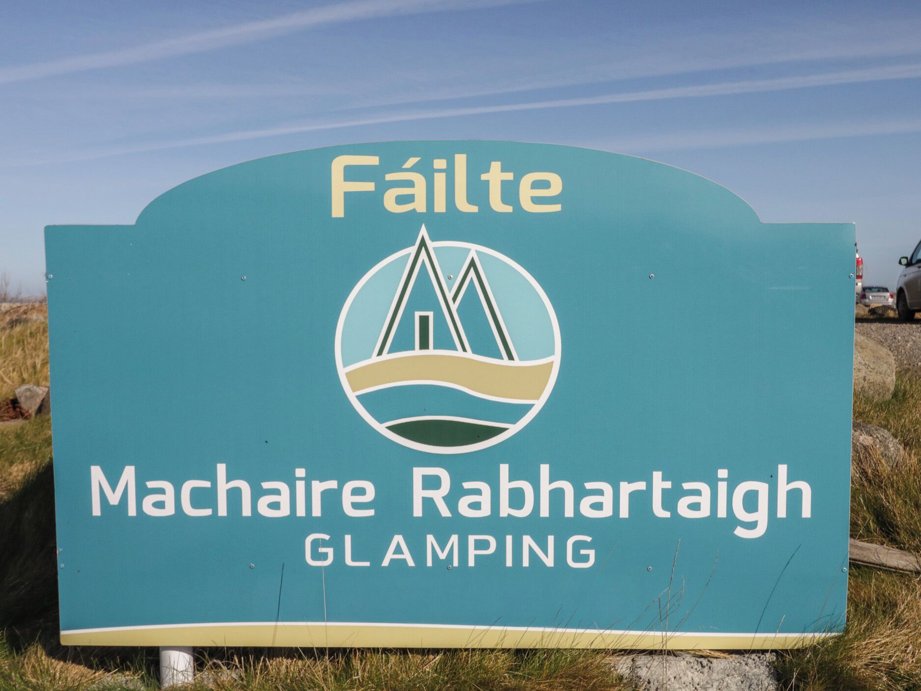 A sign with the text 'Fáilte' and 'Machaire Rabhrataigh GLAMPING' indicating a location or destination.