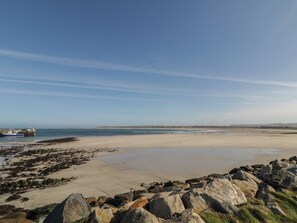 A coastal landscape with a sandy beach, rocky shoreline, and a distant view of a boat and land. - Cabin 1 Machaire Rabhartaigh (Gortahork)