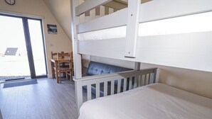A bunk bed room with a wooden desk and chair, a window, and a door leading outside. - Cabin 1 Machaire Rabhartaigh (Gortahork)