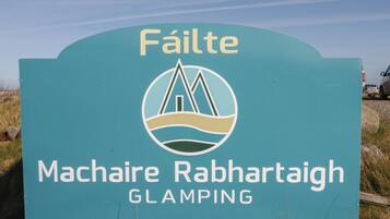 A sign with the text 'Fáilte' and 'Machaire Rabhrataigh GLAMPING' indicating a location or destination.