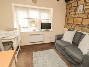 A cozy living room with a stone wall, a grey sofa, a white radiator, and a television on a windowsill. - Wren Cottage, Morpeth (Morpeth)