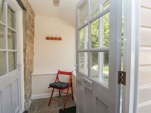 A room with a stone wall, a red chair, a white door, and a window with a view of greenery. - Wren Cottage, Morpeth (Morpeth)