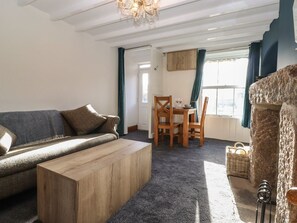 A living room with a sofa, wooden coffee table, dining table with chairs, and a stone pillar.