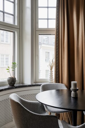A room with a round table, two chairs, a potted plant, a candle, and a view through large windows with a patterned curtain. - Modern Luxury Flat - Steps to Station (Helsinki)