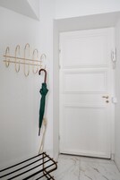 Una porta bianca con maniglia in ottone, un appendiabiti a muro con un ombrello verde e una stendibiancheria in metallo nero.