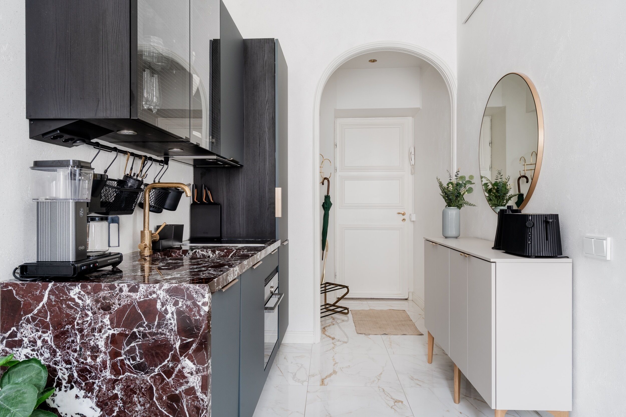 A modern kitchen with a marble countertop, black cabinets, and a stainless steel range hood.