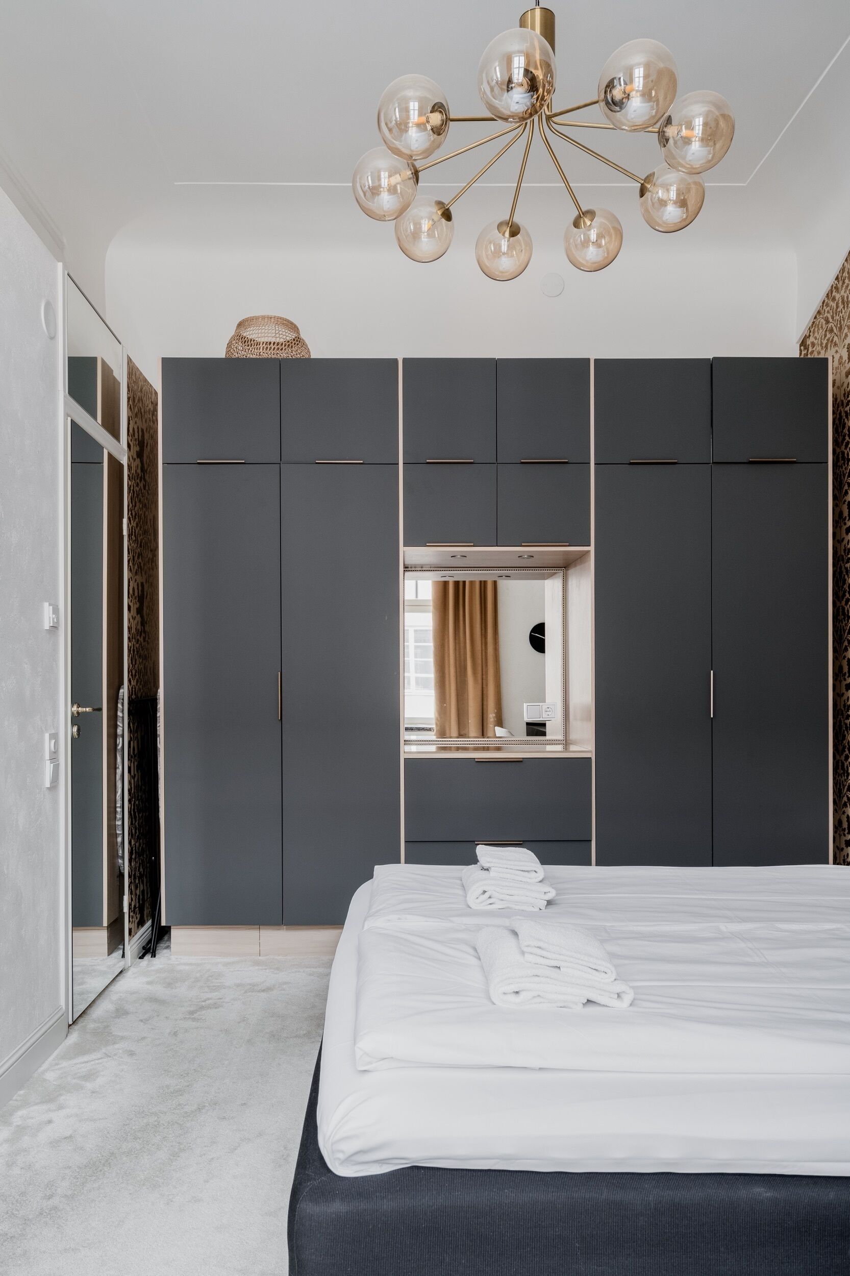 A modern bedroom with a large bed, grey wardrobe, and a chandelier.