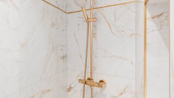 A shower with a gold showerhead and hose, set against marble walls.