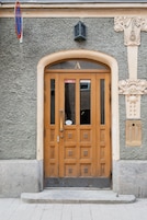 Una porta doppia in legno con un pannello di vetro, una targa sopra la porta e un muro in pietra con una colonna decorativa alla destra.