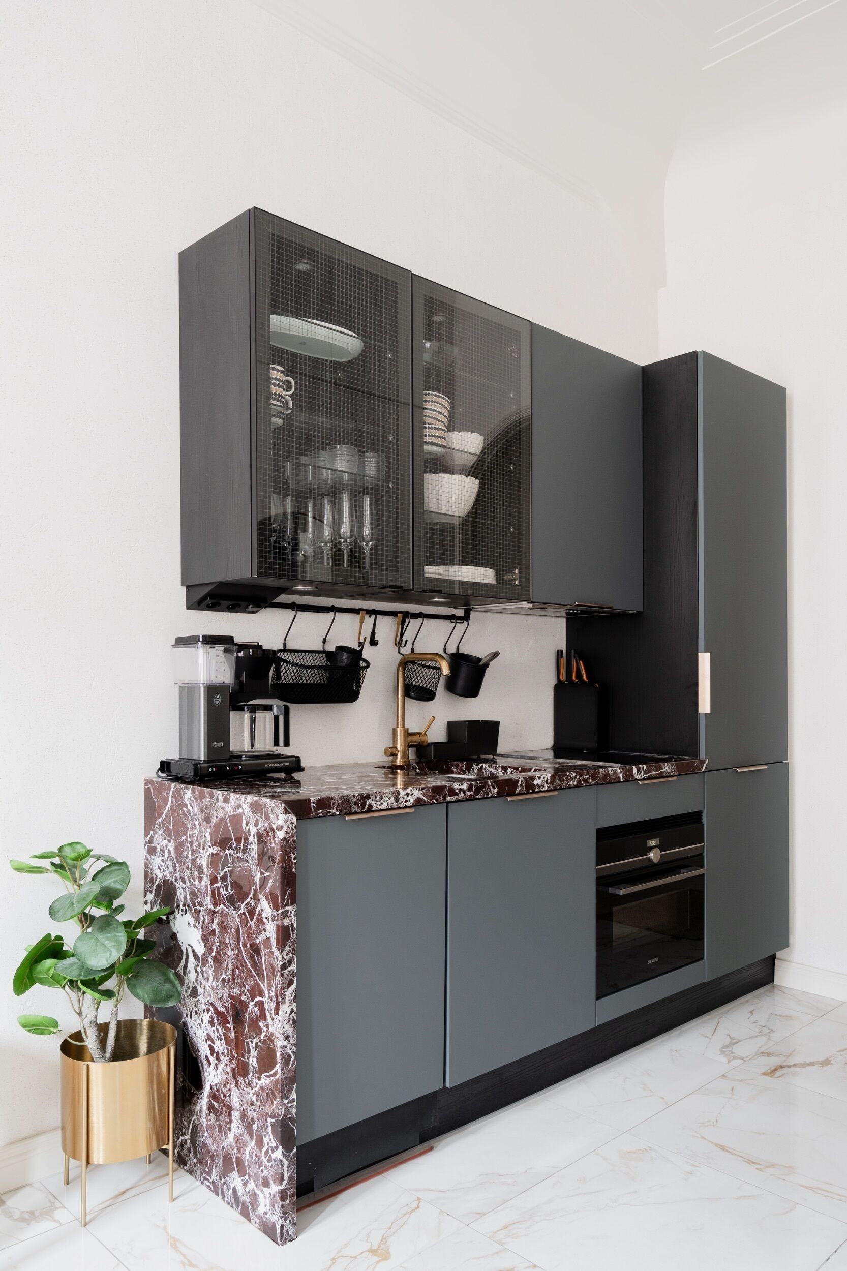 A modern kitchen with a marble countertop, black cabinets, and a coffee machine.
