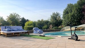 Un patio con piscina, equipo de ejercicio y sillones de descanso.