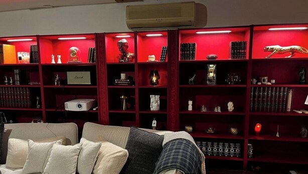 Una habitación con un sofá, una estantería iluminada con luces rojas y un ventilador de techo.