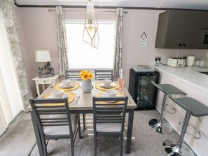 A dining area with a table set for four, a chandelier, and a kitchen area with appliances.