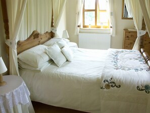Une chambre à coucher avec un lit à baldaquin, une table de chevet avec une lampe, une fenêtre avec des rideaux et une commode.