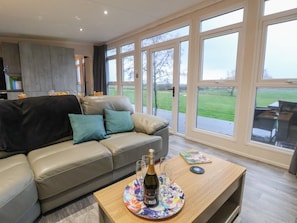Ein modernes Wohnzimmer mit einer Couch, einem Couchtisch mit Flasche und Gläsern sowie großen Fenstern mit Blick ins Freie.