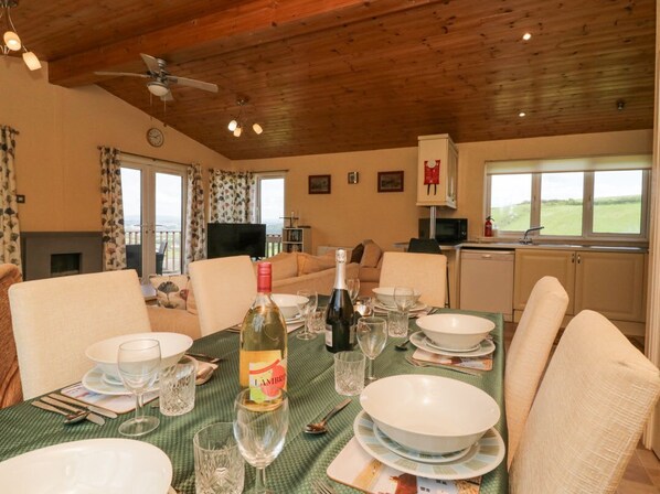 A dining area with a table set for four, a bottle of wine, and a television in the background.