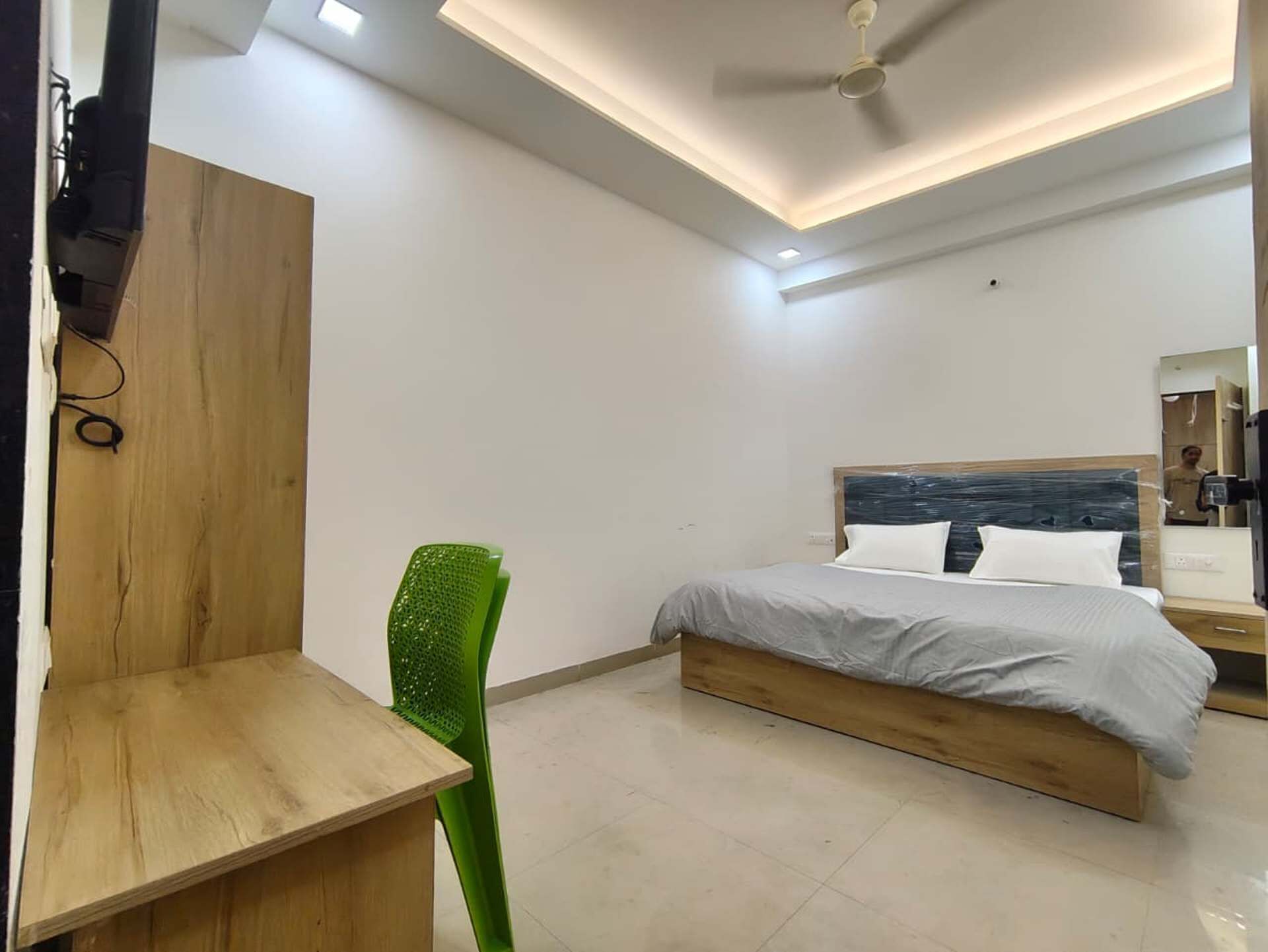 A modern bedroom with a wooden bed frame, a green chair, and a desk.