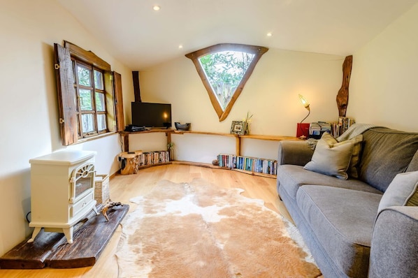 Una sala de estar acogedora con un sofá, un televisor, estanterías de madera y un ventanal triangular original.