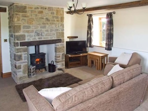 A cozy living room with a stone fireplace, a television, a sofa, and a window with curtains. - Swallows Barn, Cressbrook (Buxton)