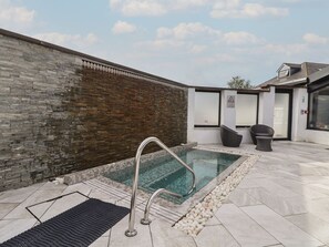 A spa area with a stone wall, a pool, a metal handrail, and a seating area with a chair and a table. - Lodge 3, St Asaph Denbighshire (St. Asaph)