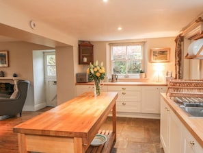A kitchen with a wooden table, white cabinets, a window, and a vase of flowers.