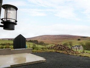 A rural landscape with a black shed, a pile of logs, and a house in the background.