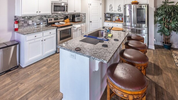 A modern kitchen with white cabinets, stainless steel appliances, a granite countertop, and a central island with stools. - Hideaway Getaway - Statham (Statham)