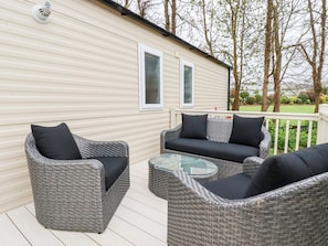 A wicker outdoor seating area with a glass table, adjacent to a mobile home with two windows. - The Mermaid A04, Par, Cornwall (Par)