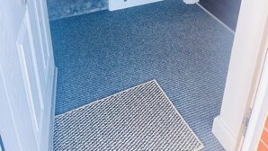 Un escalier menant à un palier où se trouve un radiateur blanc, une petite étagère ornée d’objets décoratifs et une porte dotée d’un panneau de verre.
