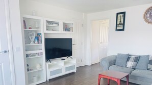Un salon avec un téléviseur à écran plat posé sur un meuble de télévision blanc, un canapé gris agrémenté de coussins à motifs et une table basse rouge.