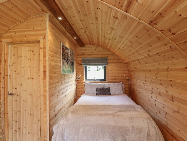 A cozy wooden cabin room with a bed, a window, and a door.