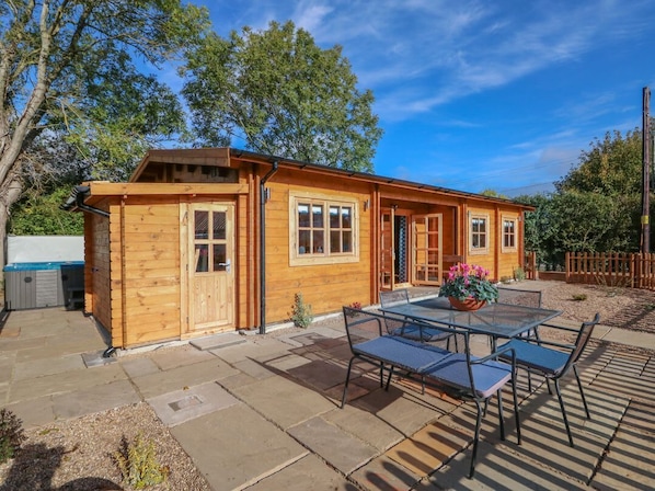Una cabaña de madera con un patio, una mesa y sillas, y una maceta.